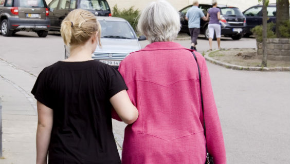 Yngre person går arm i arm med ældre person på en parkeringsplads med poser i hånden